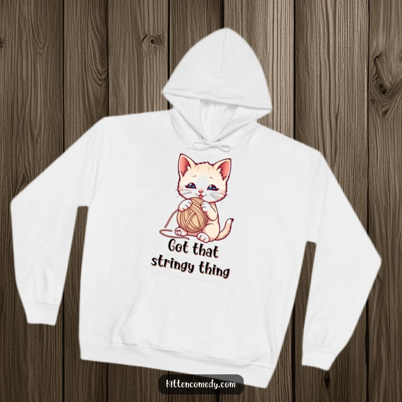 Funny kitten playfully batting at a yarn ball on a cozy hoodie, perfect for cat enthusiasts.