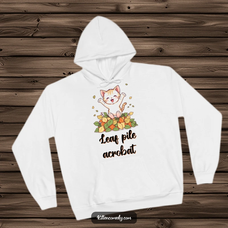 Funny kitten hoodie showing a playful cat joyfully leaping into a large pile of colorful autumn leaves, celebrating the fall season.