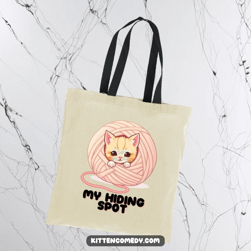 Funny kitten tote bag showing a mischievous kitten peeking from behind a giant yarn ball, perfect for carrying items with humor.